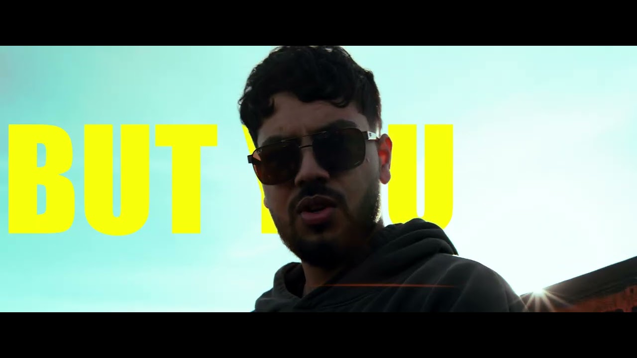 A man in sunglasses stands before large yellow text.