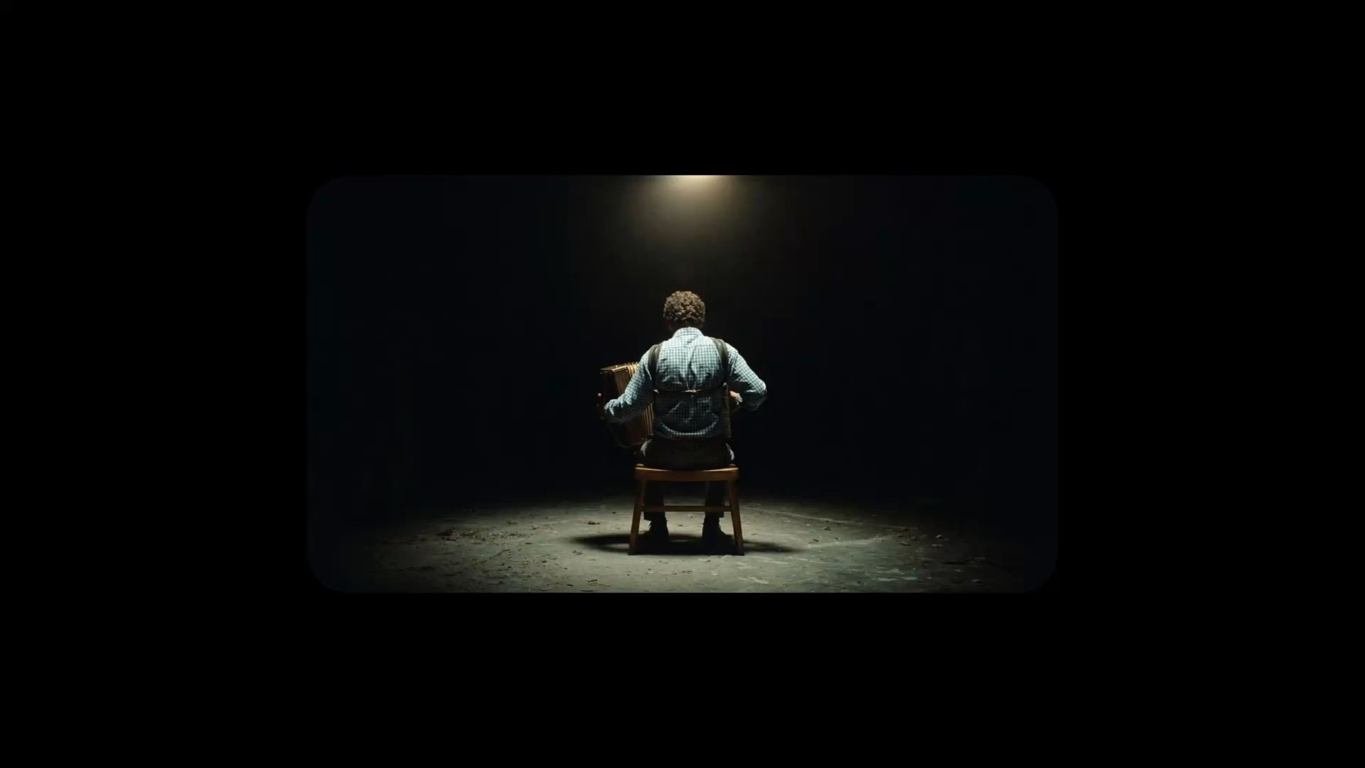 An accordion player sits under a single spotlight.
